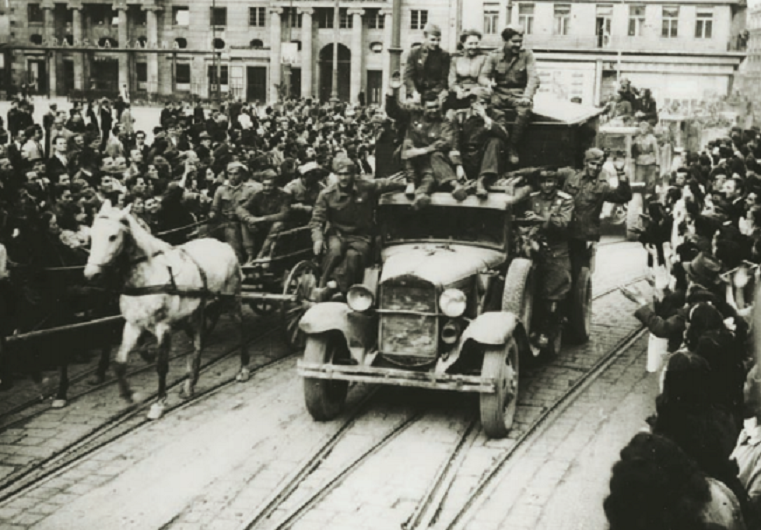 Kroz masu okupljenih građana iz Jurišićeve ulice na Trg pristiže kolona partizanskih kamiona i zaprežnih vozila s partizanima 