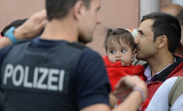 Refugee (R) with child on his arm waits for a special train at the railway station in Freilassing, near the Austrian-German border, southern Germany, on September 15, 2015, after changing from an express train coming from Hungary and Austria. Around 2,000 migrants have crossed into the southern state of Bavaria since Germany announced its policy U-turn on September 13, 2015, federal police said on September 15, albeit at a slower pace than in recent weeks. AFP PHOTO / CHRISTOF STACHE