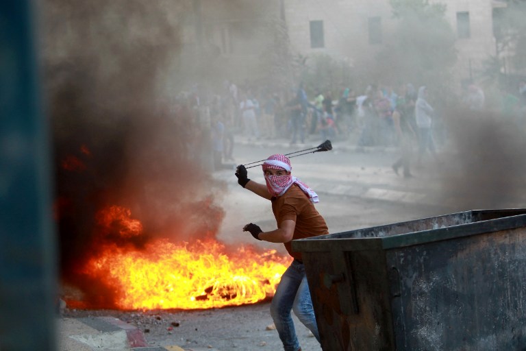 A Palestinian youth uses a slingshot to throw stones towards Israeli security forces (unseen) during clashes at the main entrance of the West Bank town of Bethlehem on October 6, 2015, following the funeral of 13-year-old Palestinian Abdel Rahman Abdullah. The Israeli army shot dead the Palestinian youth during clashes at a refugee camp near Bethlehem on October 5 as violence spiked in east Jerusalem and the occupied West Bank. AFP PHOTO / MUSA AL-SHAER