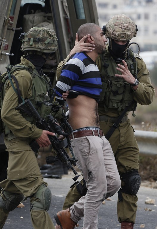 Israeli soldiers detain a Palestinian stone thrower during clashes in Beit El, on the outskirts of the West Bank city of Ramallah, on October 7, 2015. New violence rocked Israel and the Israeli-occupied West Bank, including a stabbing in annexed east Jerusalem, even as Israel and Palestinian president Mahmud Abbas took steps to ease tensions. AFP PHOTO / ABBAS MOMANI