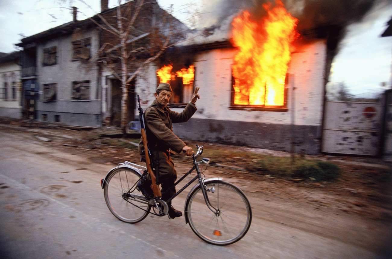 Soldiers and Paramilitaries - A Serbian soldier cycles by a burning house on the destroyed streets of the Croatian city of Vukovar, Nov. 24, 1991. The city was completely destroyed after three months of bombing by Serbian forces., Image: 116177603, License: Rights-managed, Restrictions: Content available for editorial use, pre-approval required for all other uses. This content not available to be downloaded through Quick Pic Not available for license and invoicing to customers located in the Czech Republic. Not available for license and invoicing to customers located in the Netherlands. Not available for license and invoicing to customers located in India. Not available for license and invoicing to customers located in Finland. Not available for license and invoicing to customers located in Italy., Model Release: no, Credit line: Profimedia, Corbis VII