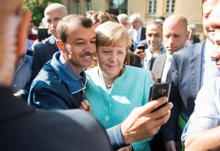 (FILES) This file photo taken on September 10, 2015 shows an asylum seeker (C, L) taking a selfie picture with German Chancellor Angela Merkel (C, R) following Merkel's visit at a branch of the Federal Office for Migration and Refugees and a camp for asylum-seekers in Berlin. AFP journalists have chosen Angela Merkel as the most influential figure of 2015 after the German chancellor stamped her mark on the European migrant and Greek financial crises. The chancellor's open-door policy brought around a million refugees to Germany over 2015. The flood of migrants, a consequence of the devastating war in Syria, was the biggest in Europe since World War II and put the continent under huge strain, exposing its fault lines. / AFP / DPA / BERND VON JUTRCZENCKA