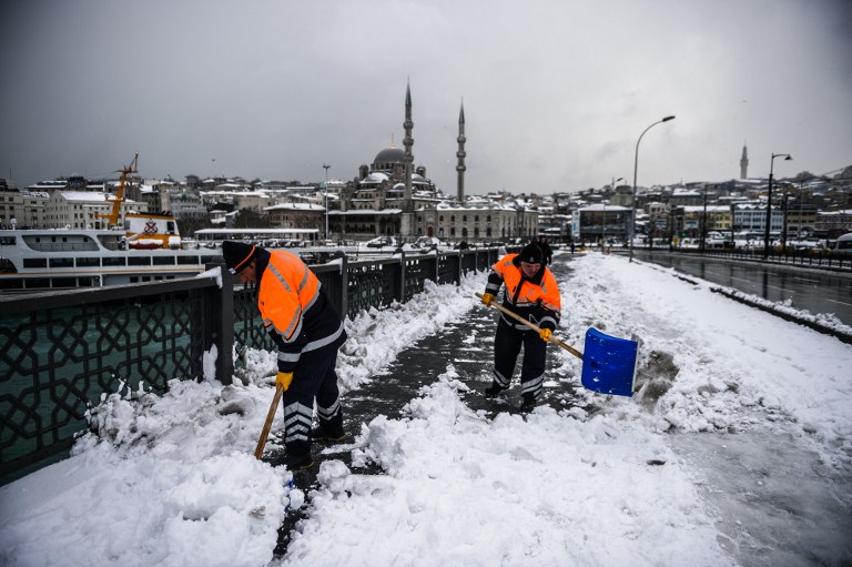 Municipality workers shovel snow from a pavement during a snowfall in Istanbul on December 31, 2015. Istanbul governors office has urged people to avoid going outside unless necessary, citing expectation of heavy snowfall until January 2, 2016. / AFP / OZAN KOSE