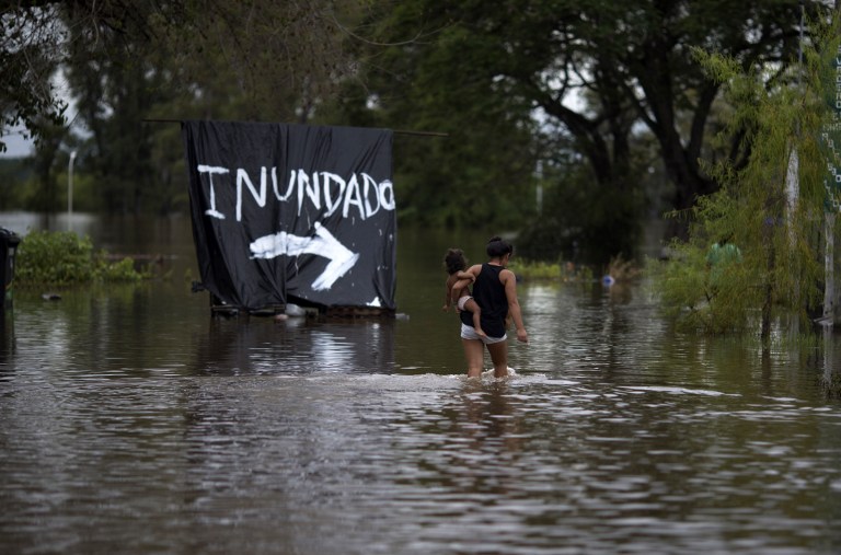 A woman carries her baby through a flooded area of Concordia, Entre Rios province, Argentina, on December 29, 2015. Over recent days the storms blamed on the "El Nino" weather phenomenon have killed four people in Brazil and two in Argentina. Officials say rainfall has driven at least 160,000 people from their homes in Paraguay, Argentina and Uruguay. AFP PHOTO/STR / AFP / STR