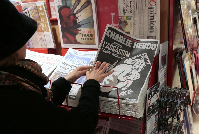 A woman looks at the special commemorative edition of French satirical newspaper Charlie Hebdo at a newsstand in Paris, on January 6, 2015, to mark the one-year anniversary of the jihadist attack that claimed the lives of 12 people, including three of its best-known cartoonists. True to form, the cover is unabashedly provocative, featuring a Kalashnikov-toting God figure wearing a blood-stained white robe, under the headline: "One year on: The killer is still at large." / AFP / JACQUES DEMARTHON