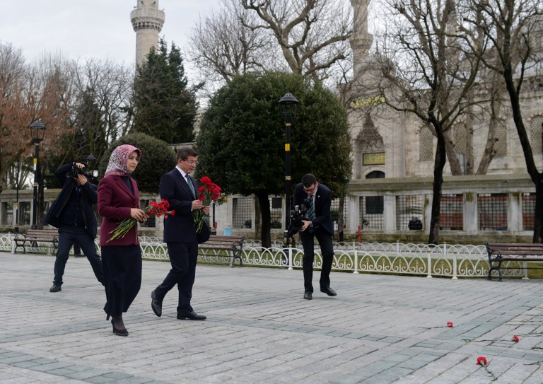 Turkish Prime Minister Ahmet Davutoglu (R) and his wife Sare Davutoglu arrive to place flowers in tribute to the victims at the site of yesterday's attack in the city's tourist hub of Sultanahmet on January 13, 2016 in Istanbul. Turkish authorities probed how a jihadist from Syria killed 10 mainly German tourists in an attack in the heart of Istanbul that raised alarm over security in the city. / AFP / BULENT KILIC