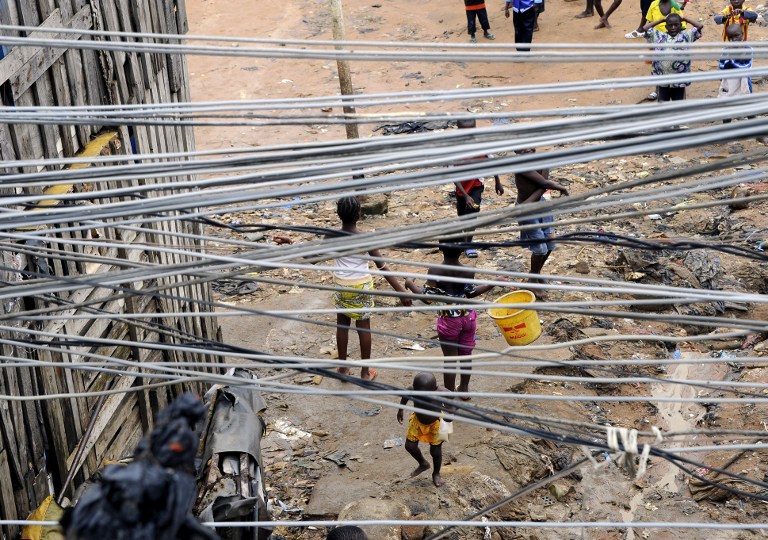 Children stand near a common courtyard under a bunch of electric lines, on June 19, 2014 in a poor neighborhood in the Attecoube commune, central part of Abidjan. Twelve people were killed during the night between June 18 and June 19 in landslides after heavy rains struck the Ivorian capital. The total number of victims who have died in such circumstances reached twenty-three since the beginning of the rainy season about fifteen days ago. AFP PHOTO / SIA KAMBOU / AFP / SIA KAMBOU