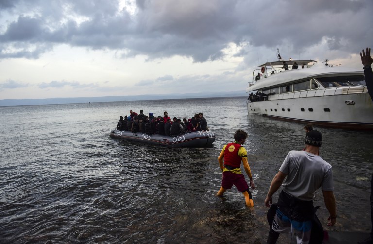 Migrants and refugees arrive on a rubber dinghy and a boat (back) on the Greek island of Lesbos after crossing the Aegean Sea from Turkey on November 21, 2015. European Health Commissioner Vytenis Andriukaitis on November 19 said resources were urgently needed on the Greek island of Lesbos where hundreds of migrants continue to land daily from neighbouring Turkey. AFP PHOTO / BULENT KILIC / AFP / BULENT KILIC