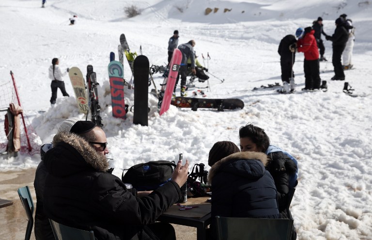 Jewish people take a break at the terrace of a cafe at the Israeli Mount Hermon ski resort, in the Israeli-occupied Golan Heights, on January 21, 2016. For Israelis, the Hermon range, straddling Lebanon and the Syrian and Israeli-held sectors of the Golan, is a highly strategic area under close surveillance. / AFP / THOMAS COEX / TO GO WITH AFP STORY BY DAPHNE ROUSSEAU