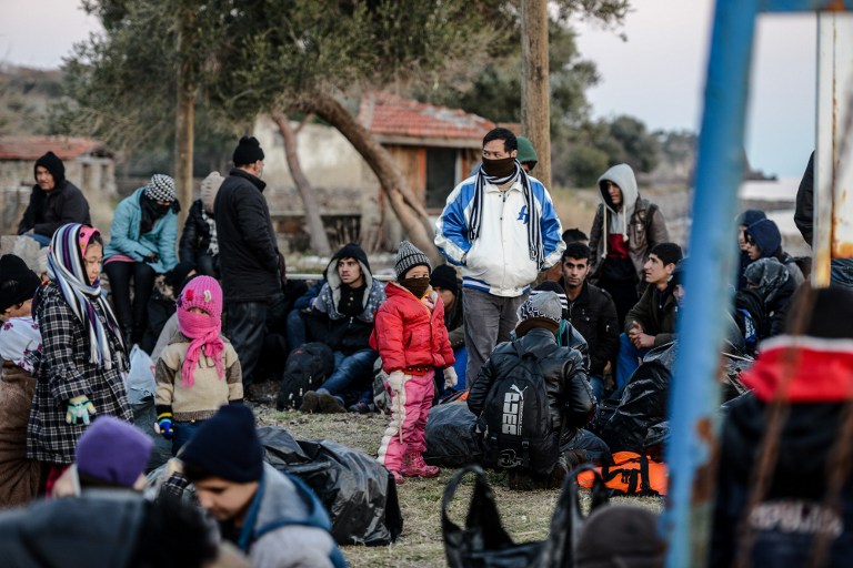 Syrian and Afghan migrants and refugees wait after being caught by Turkish gendarme on January 27, 2016 at Canakkale's Kucukkuyu district The European Commission said Greece could face border controls with the rest of the EU's passport-free Schengen zone if it fails to secure its exterior borders, with thousands of migrants still landing on Greek beaches from Turkey day after day. / AFP / OZAN KOSE