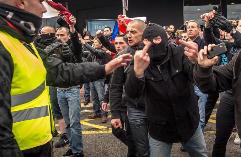 A supporter of the Pegida movement (Patriotic Europeans Against the Islamisation of the Occident) wearing a balaclava gives the finger during a banned demonstration in Calais, northern France, on February 6, 2016. Around 20 anti-migrant protesters were arrested in the French port of Calais after scuffles with police at a banned rally in support of a Europe-wide initiative by the Islamophobic Pegida movement. / AFP / PHILIPPE HUGUEN