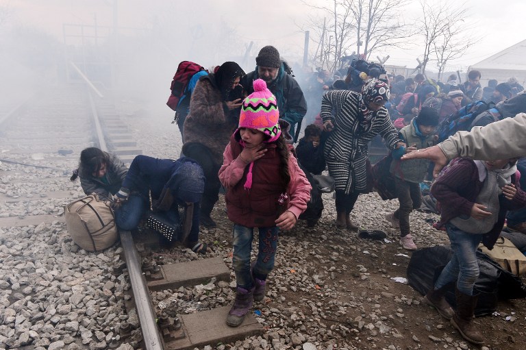 A child coughs as migrants and refugees run away after Macedonian police fired tear gas at hundreds of Iraqi and Syrian migrants who tried to break through the Greek border fence in Idomeni, on February 29, 2016. Greek police said more than 6,000 people were massed at the border, in a buildup triggered by Austria and Balkan states capping the numbers of migrants entering their territory. / AFP / LOUISA GOULIAMAKI
