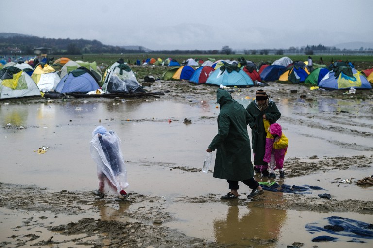 A migrant family walks on a muddy field on March 10, 2016, at a makeshift camp of the Greek-Macedonian border, near the Greek village of Idomeni, where thousands of refugees and migrants are stranded by the Balkan border blockade. The main migrant trail from Greece to northern Europe was blocked March 9 after western Balkan nations slammed shut their borders, hiking pressure for an EU-Turkey deal and exacerbating a dire situation on the Macedonian border. More than 14,000 mainly Syrian and Iraqi refugees are camping out by the northern Idomeni border crossing with Macedonia -- many of them for weeks -- at a muddy, unhygienic camp operated by beleaguered aid groups. / AFP / DIMITAR DILKOFF