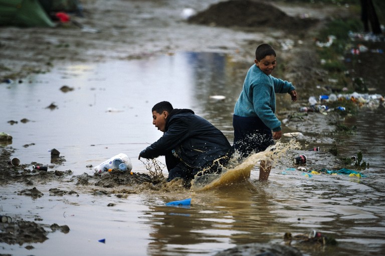 Migrant children play in a muddy puddle on March 10, 2016, at a makeshift camp of the Greek-Macedonian border, near the Greek village of Idomeni, where thousands of refugees and migrants are stranded by the Balkan border blockade. The main migrant trail from Greece to northern Europe was blocked March 9 after western Balkan nations slammed shut their borders, hiking pressure for an EU-Turkey deal and exacerbating a dire situation on the Macedonian border. More than 14,000 mainly Syrian and Iraqi refugees are camping out by the northern Idomeni border crossing with Macedonia -- many of them for weeks -- at a muddy, unhygienic camp operated by beleaguered aid groups. / AFP / DIMITAR DILKOFF