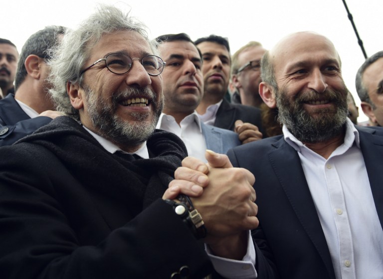 Turkish daily Cumhuriyet's editor-in-chief Can Dundar (L) and Ankara editor Erdem Gul (R) hold hands as they arrive at the Istanbul courthouse before his trial on March 25, 2016. Two top Turkish journalists are going on trial, accused of espionage and other serious crimes and facing possible life in prison over a story about Turkey's role in the Syrian conflict that infuriated President Recep Tayyip Erdogan. / AFP / BULENT KILIC