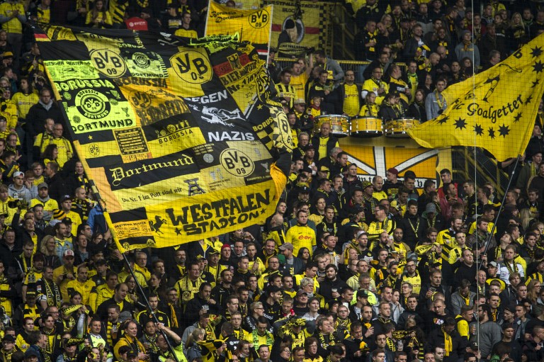Dortmund's fans wave with a giant flag reading "Against Nazi" prior to the German first division football Bundesliga match between Borussia Dortmund and FC Augsburg on October 25, 2015 in Dortmund, western Germany. AFP PHOTO / ODD ANDERSEN RESTRICTIONS: DURING MATCH TIME: DFL RULES TO LIMIT THE ONLINE USAGE TO 15 PICTURES PER MATCH AND FORBID IMAGE SEQUENCES TO SIMULATE VIDEO. ==RESTRICTED TO EDITORIAL USE == FOR FURTHER QUERIES PLEASE CONTACT THE DFL DIRECTLY AT + 49 69 650050. / AFP / ODD ANDERSEN