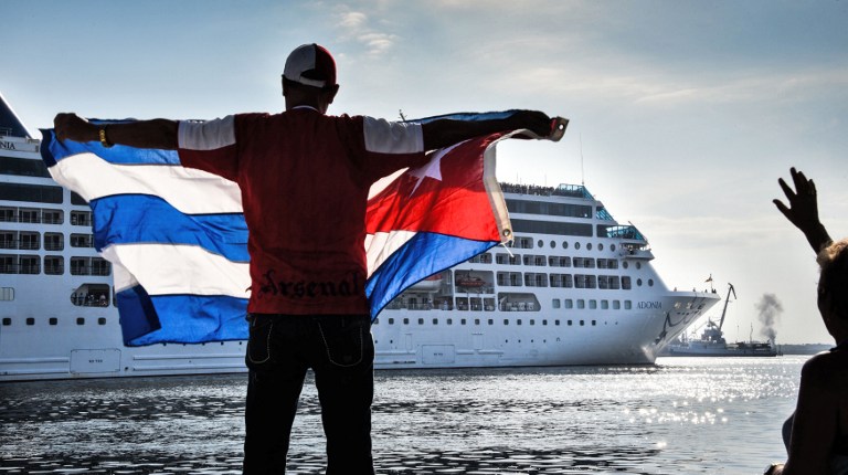 A man waves a Cuban flag at the Malecon waterfront as the first US-to-Cuba cruise ship to arrive in the island nation in decades glides into the port of Havana, on May 2, 2016. The first US cruise ship bound for Cuba in half a century, the Adonia -- a vessel from the Carnival cruise's Fathom line -- set sail from Florida on Sunday, marking a new milestone in the rapprochement between Washington and Havana. The ship -- with 700 passengers aboard -- departed from Miami, the heart of the Cuban diaspora in the United States. / AFP PHOTO / ADALBERTO ROQUE