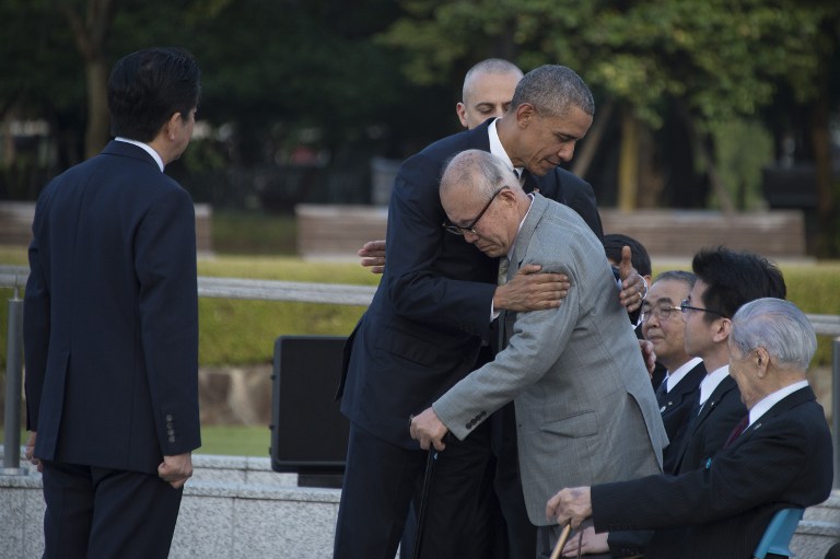 Japan's Prime Minister Shinzo Abe (L) looks on as US President Barack Obama (centre L) hugs a survivor (centre R) of the 1945 atomic bombing of Hiroshima, during a visit to the Hiroshima Peace Memorial Park on May 27, 2016. Obama on May 27 paid moving tribute to victims of the world's first nuclear attack. / AFP PHOTO / Jim Watson
