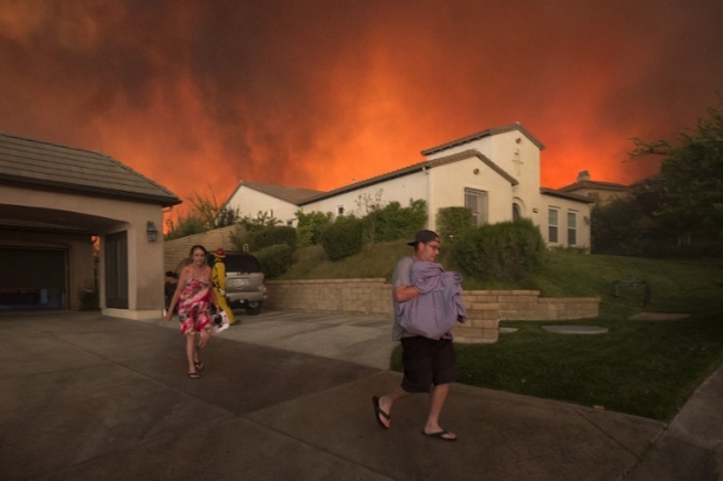 Residents flee their home as flames from the Sand Fire close in on July 23 2016 near Santa Clarita, California. Fueled by temperatures reaching about 108 degrees fahrenheit, the wildfire began yesterday has grown to 11,000 acres. / AFP PHOTO / DAVID MCNEW