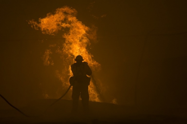A firefighter hoses down burning pipes near a water tank at the Sand Fire on July 23 2016 near Santa Clarita, California. Fueled by temperatures reaching about 108 degrees fahrenheit, the wildfire began yesterday has grown to 11,000 acres. / AFP PHOTO / DAVID MCNEW