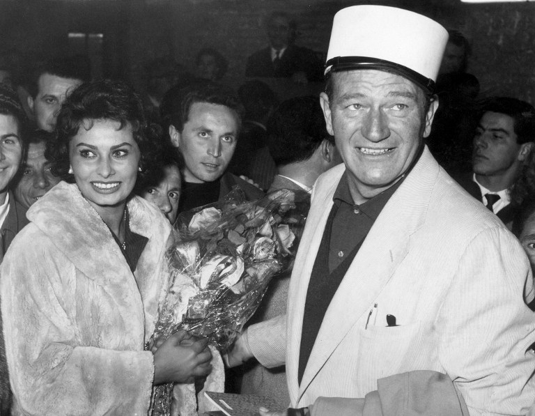 American actor John Wayne (R) and Italian actress Sophia Loren (L) arrive at Rome from Africa after the broken leg of Wayne during the shooting of "The Legend of the Lost". / AFP PHOTO / INTERCONTINENTALE / STAFF