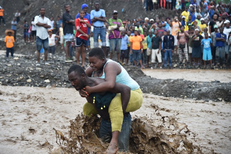 A man carries a woman across a river at Petit Goave where a bridge collapsed during the rains of the Hurricane Matthew, southwest of Port-au-Prince, October 5, 2016. Haiti and the eastern tip of Cuba -- blasted by Matthew on October 4, 2016 -- began the messy and probably grim task of assessing the storm's toll. Matthew hit them as a Category Four hurricane but has since been downgraded to three, on a scale of five, by the US National Hurricane Center. / AFP PHOTO / HECTOR RETAMAL