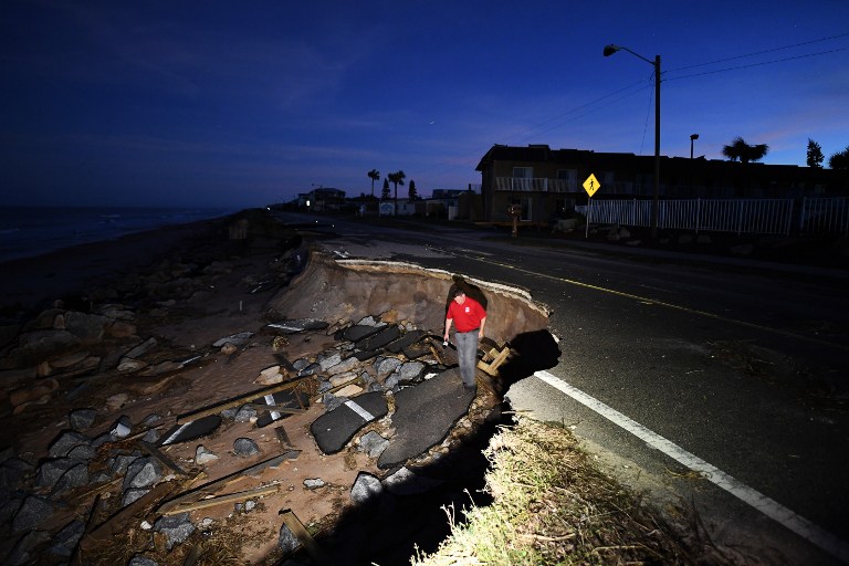 A reporter walks on the debris of a washed out highway in Flagler Beach, Florida, on October 8, 2016, after Hurricane Matthew passed the area. Hurricane Matthew weakened to a Category 1 storm Saturday as it neared the end of a four-day rampage that left a trail of death and destruction across the Caribbean and up the US Atlantic coast. The full scale of the devastation in hurricane-hit rural Haiti became clear as the death toll surged past 400, three days after Hurricane Matthew leveled huge swaths of the country's south. / AFP PHOTO / Jewel SAMAD