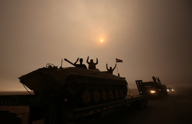 Iraqi forces flash the V-sign as they stand on an infantry fighting vehicle loaded on a truck driving through the Al-Shura area, south of Mosul, on October 24, 2016, during an operation to retake the main hub city from the Islamic State (IS) group jihadists. Iraqi forces advancing on Mosul faced stiff resistance from the Islamic State group on October 24 despite the US-led coalition unleashing an unprecedented wave of air strikes to support the week-old offensive. Federal forces and Kurdish peshmerga fighters were moving forward in several areas, AFP correspondents on various fronts said, but the jihadists were hitting back with shelling, sniper fire, suicide car bombs and booby traps. / AFP PHOTO / AHMAD AL-RUBAYE