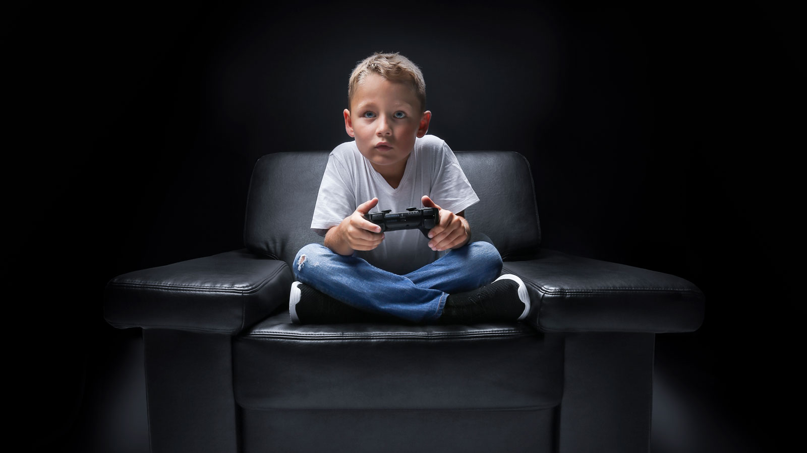Djete sjedi na fotelji u mraku i igra video igre