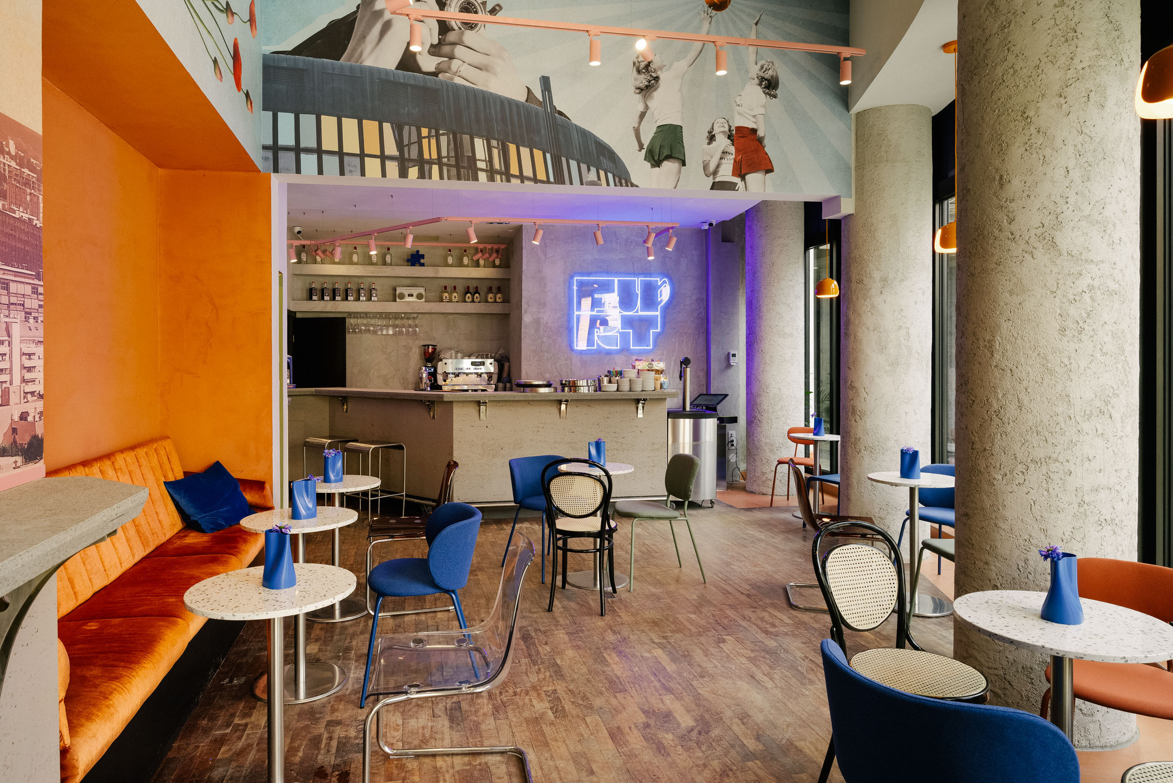 Moderna kavana s plavim neonskim natpisom, narančastim sjedalima, betonskim stupovima i industrijskim dizajnom